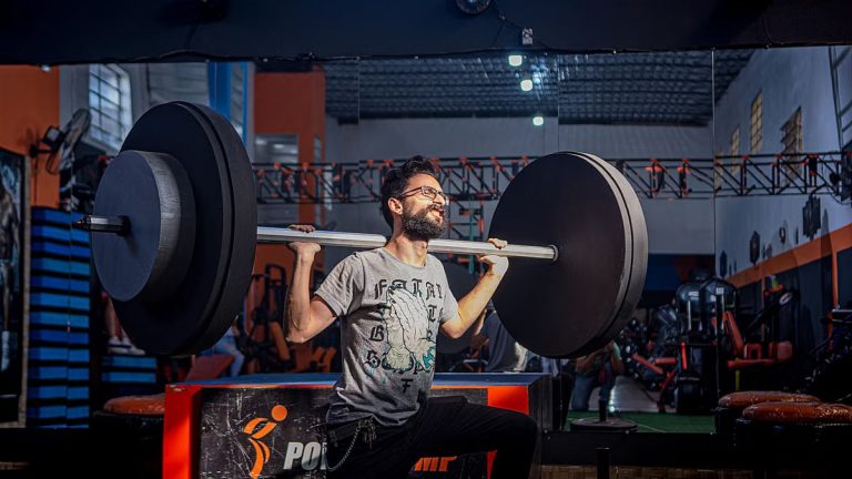 Adult male lifting a barbell in a gym, showcasing strength and fitness.